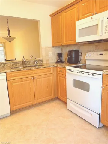 Kitchen featuring sink, tasteful backsplash, light stone counters, white appliances, and light tile patterned flooring
