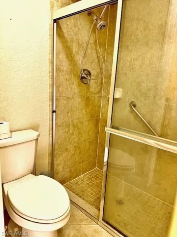 Bathroom featuring a shower with shower door, tile patterned floors, and toilet