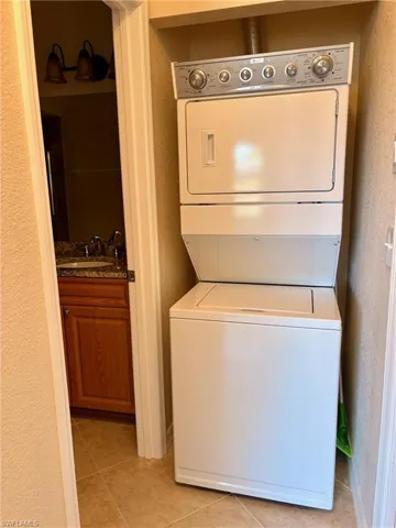 Clothes washing area featuring sink, light tile patterned floors, and stacked washer / dryer