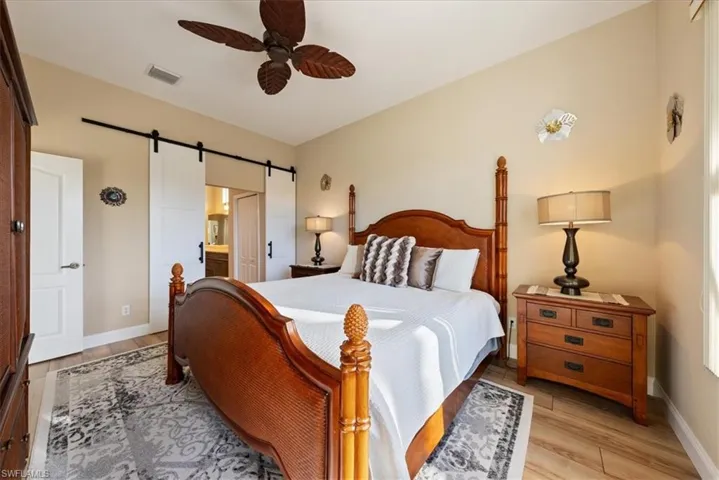 Bedroom featuring ceiling fan, ensuite bath, a barn door, and light hardwood / wood-style floors