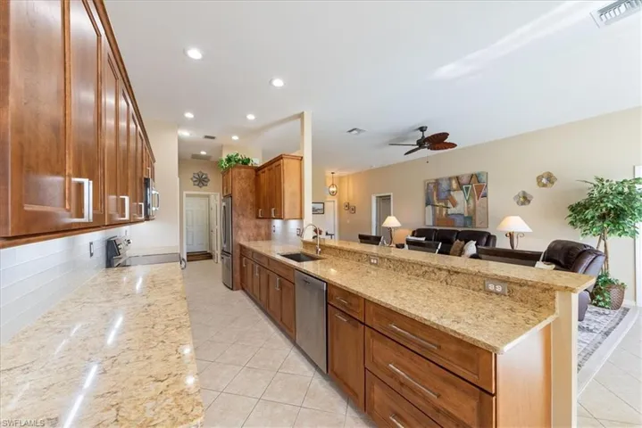 Kitchen with sink, ceiling fan, appliances with stainless steel finishes, light stone countertops, and kitchen peninsula