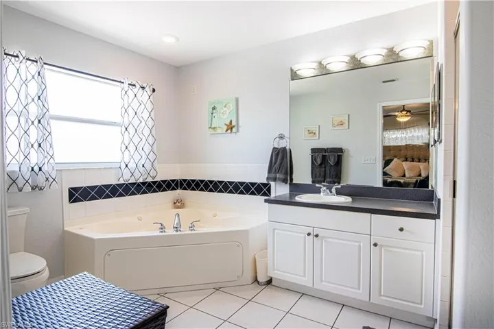 Bathroom with ceiling fan, tile floors, a washtub, toilet, and large vanity