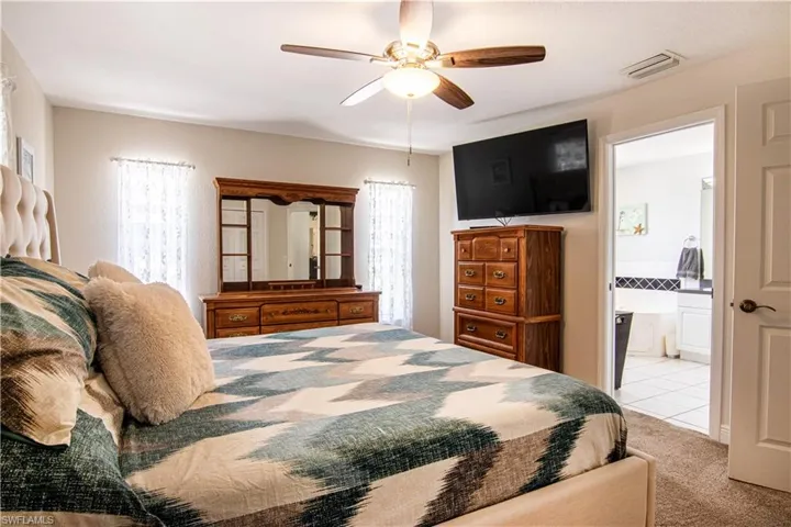 Bedroom with light carpet, connected bathroom, and ceiling fan