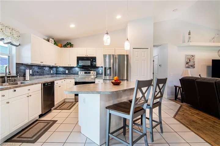 Kitchen with vaulted ceiling, light wood-type flooring, black appliances, a kitchen island, and backsplash