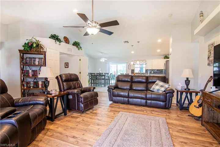 Living room featuring lofted ceiling, light wood-type flooring, and ceiling fan with notable chandelier