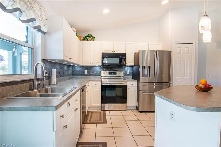 Kitchen featuring stainless steel appliances, white cabinets, decorative light fixtures, sink, and light tile floors