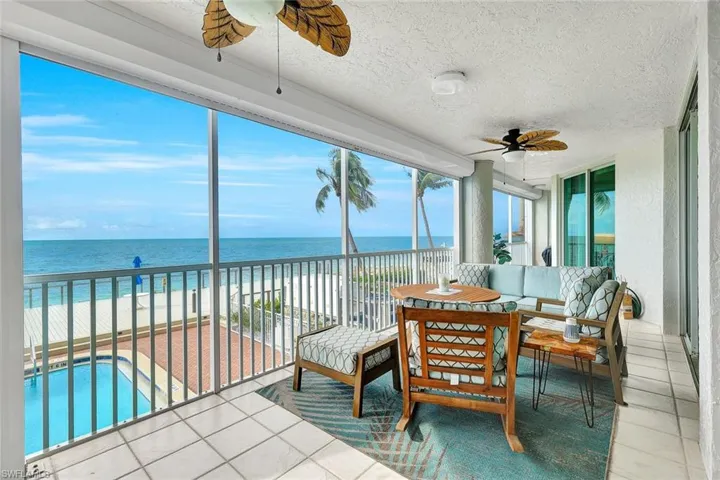 Screened-in balcony featuring tile flooring, ceiling fans, and metal railings, overlooking the ocean, pool, and deck