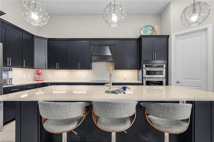 Kitchen featuring dark cabinets, a breakfast bar area, light stone counters, and a kitchen island with sink