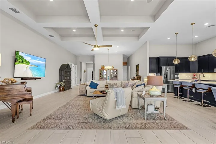 Living area featuring coffered ceiling, light wood-style floors, ceiling fan, and hanging lights