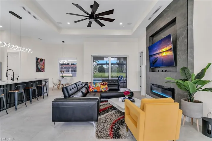 Living area featuring a tray ceiling, a large fireplace, a ceiling fan, and visible vents