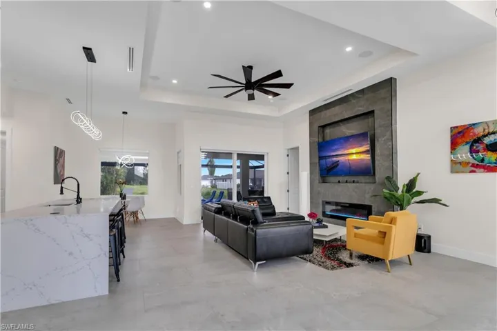 Living room with a raised ceiling, ceiling fan, baseboards, and recessed lighting