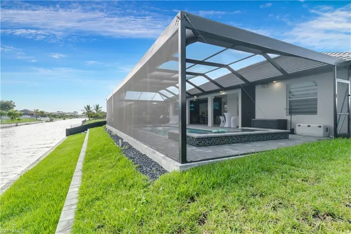 Rear view of house featuring an in ground hot tub, a lanai, a lawn, an outdoor pool, and a patio area