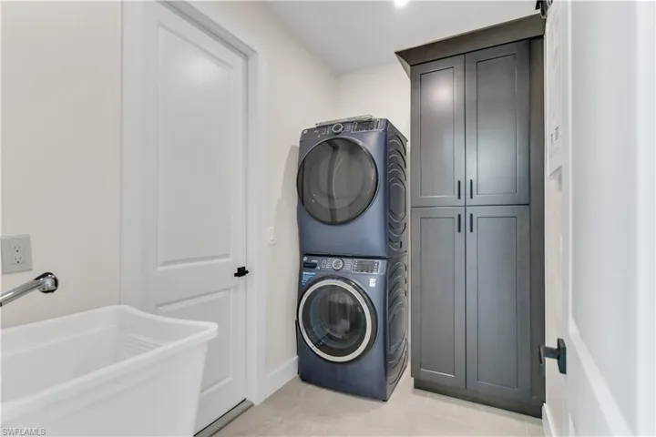 Laundry room featuring cabinet space, stacked washer / drying machine, a sink, baseboards, and light tile patterned floors