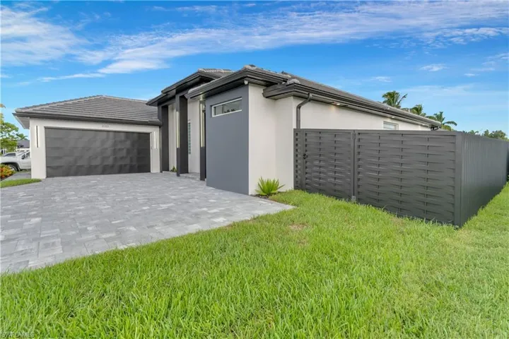 View of front facade with fence, stucco siding, decorative driveway, and a front yard