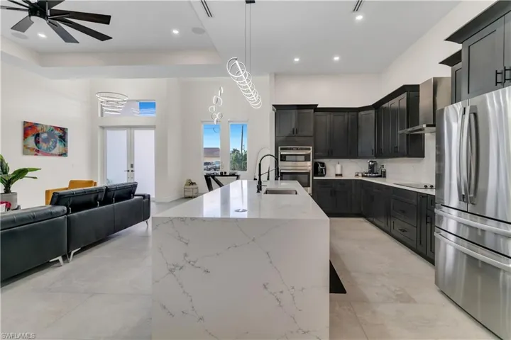Kitchen with a kitchen island with sink, open floor plan, wall chimney range hood, light stone counters, and appliances with stainless steel finishes