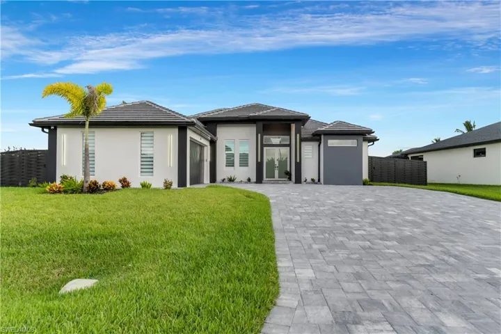 Prairie-style house featuring stucco siding, decorative driveway, fence, and a front lawn