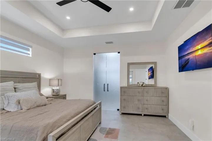 Bedroom featuring a ceiling fan, baseboards, visible vents, and a tray ceiling