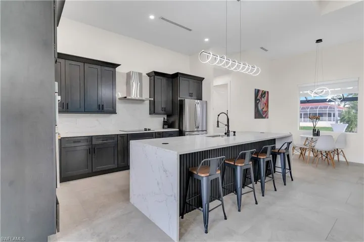 Kitchen featuring freestanding refrigerator, a kitchen island with sink, a breakfast bar area, wall chimney range hood, and a sink
