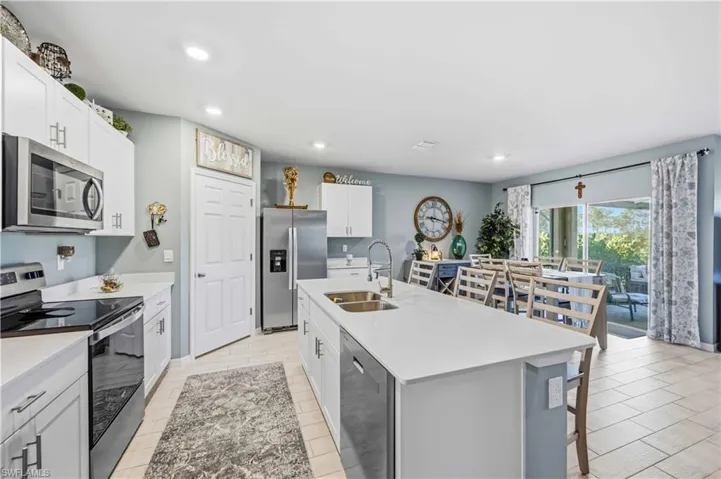 Open-concept kitchen featuring an oversized island, stainless steel appliances, white cabinetry, and light-toned tile flooring