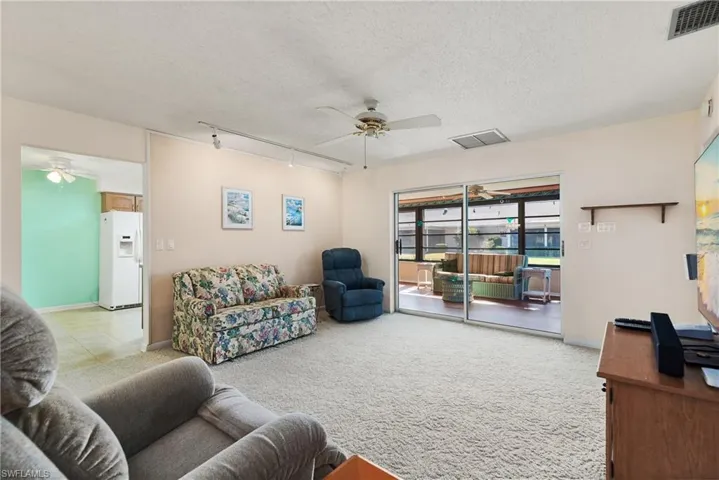 Living room with track lighting, a ceiling fan, a textured ceiling, and light colored carpet