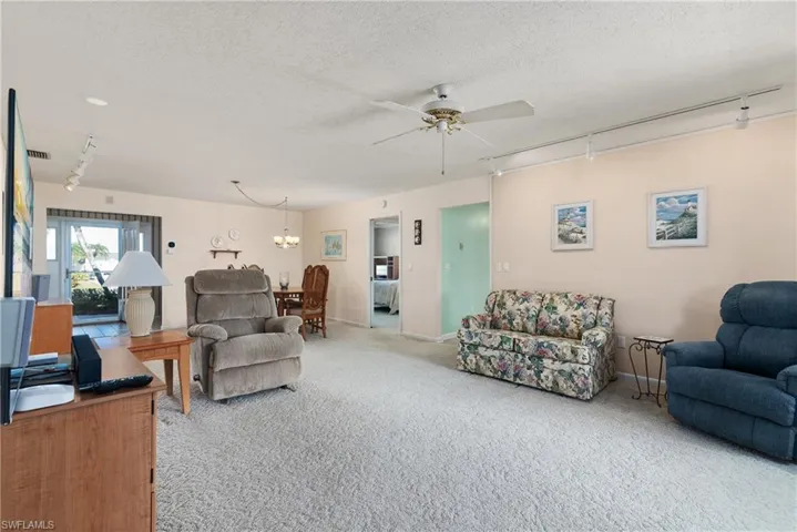 Carpeted living area featuring track lighting, ceiling fan, a chandelier, and a textured ceiling