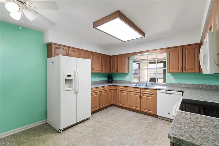 Kitchen with white appliances, brown cabinets, light flooring, and a ceiling fan