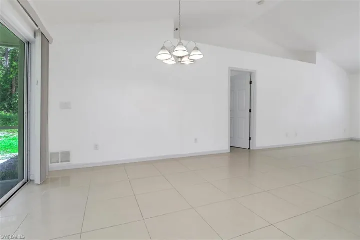 Tiled spare room featuring lofted ceiling, plenty of natural light, and a chandelier