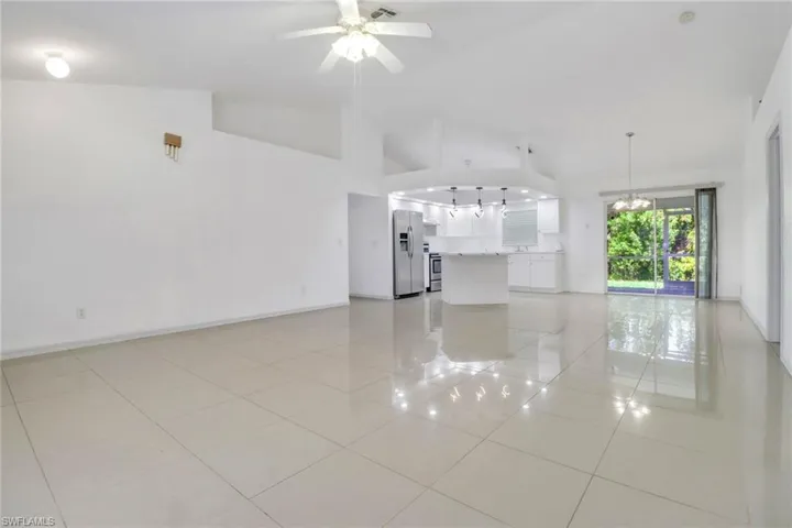 Unfurnished living room featuring light tile patterned floors, a ceiling fan, a chandelier, and high vaulted ceiling