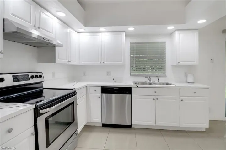 Kitchen with stainless steel appliances, under cabinet range hood, recessed lighting, light tile patterned flooring, and white cabinets