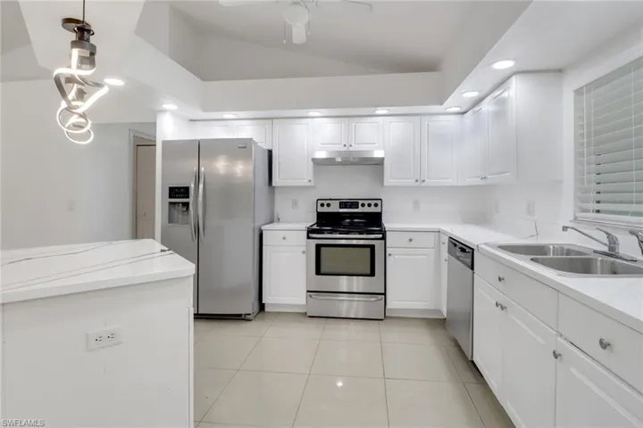 Kitchen featuring appliances with stainless steel finishes, under cabinet range hood, lofted ceiling, white cabinetry, and recessed lighting