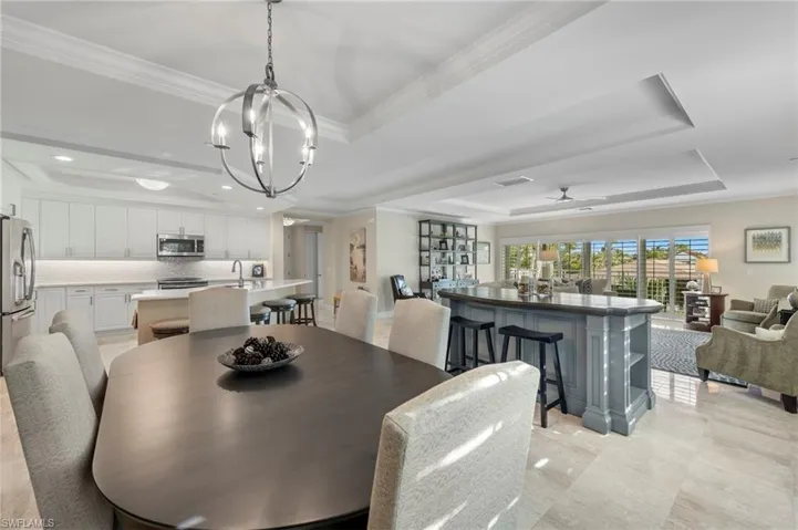 Dining space featuring light tile patterned flooring, crown molding, a tray ceiling, and ceiling fan with notable chandelier