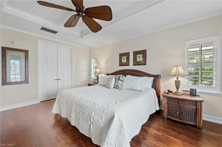 Bedroom with crown molding, dark hardwood / wood-style flooring, ceiling fan, a raised ceiling, and a closet
