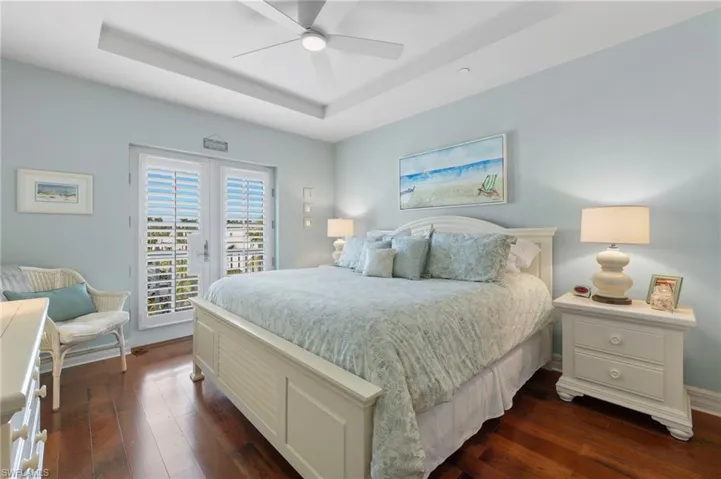Bedroom featuring french doors, ceiling fan, access to outside, dark hardwood / wood-style floors, and a tray ceiling