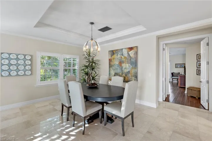 Dining area with an inviting chandelier, hardwood / wood-style flooring, a raised ceiling, and crown molding