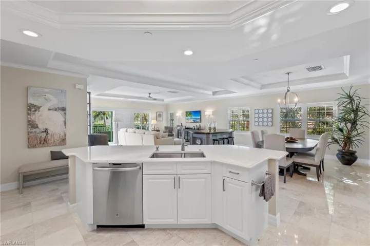Kitchen featuring stainless steel dishwasher, a kitchen island with sink, a tray ceiling, and a wealth of natural light