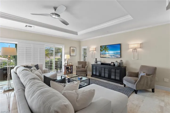 Living room with ceiling fan, a raised ceiling, and ornamental molding