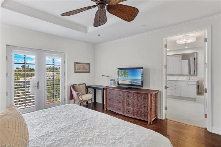 Bedroom with ensuite bathroom, a tray ceiling, french doors, dark wood-type flooring, and ceiling fan
