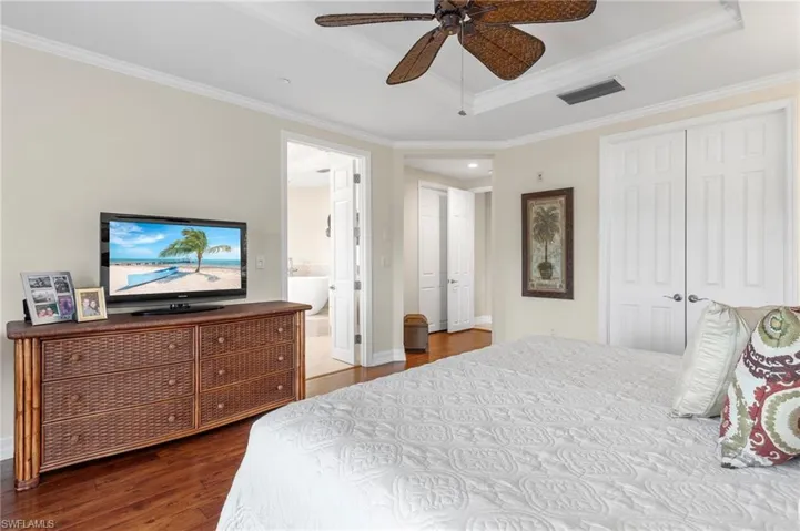 Bedroom featuring ceiling fan, a tray ceiling, crown molding, dark hardwood / wood-style floors, and ensuite bathroom