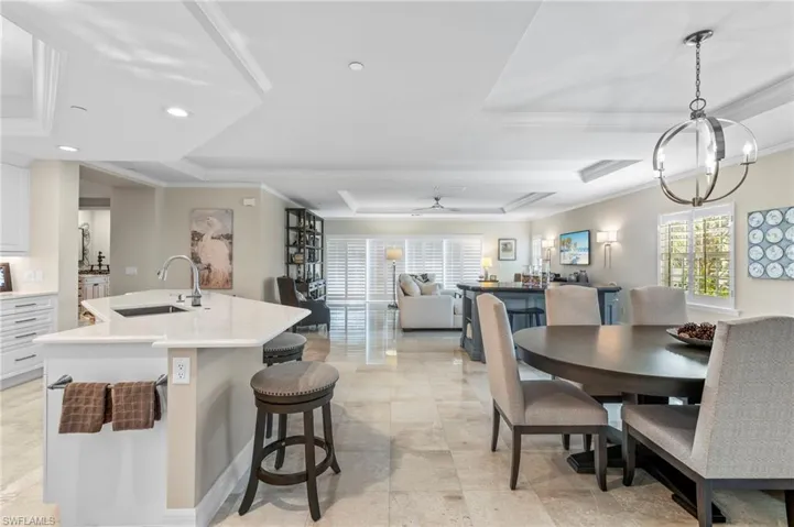 Dining space with ceiling fan with notable chandelier, ornamental molding, sink, a raised ceiling, and light tile patterned floors