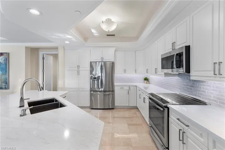 Kitchen featuring a tray ceiling, decorative backsplash, white cabinets, sink, and appliances with stainless steel finishes