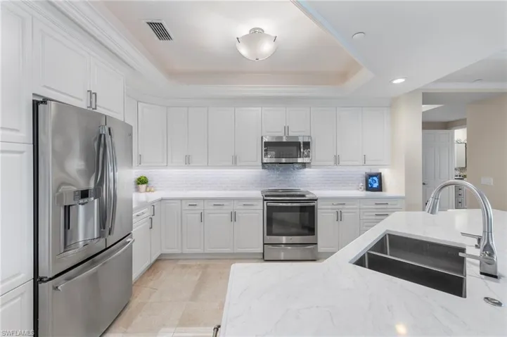 Kitchen featuring tasteful backsplash, white cabinets, appliances with stainless steel finishes, a raised ceiling, and sink