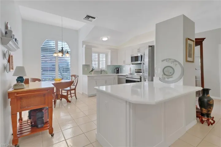 Kitchen with appliances with stainless steel finishes, white cabinets, decorative light fixtures, kitchen peninsula, and a chandelier