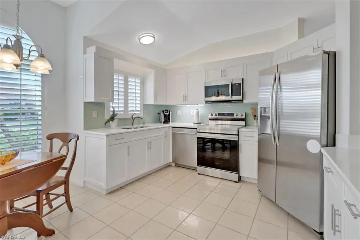 Kitchen with white cabinetry, sink, decorative light fixtures, and stainless steel appliances