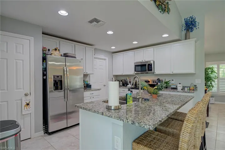Kitchen featuring stainless steel appliances, light tile patterned floors, white cabinetry, recessed lighting, and granite counters
