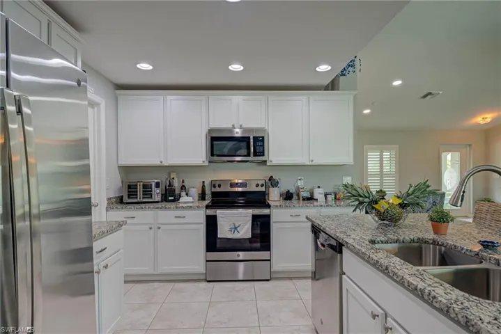 Kitchen with appliances with stainless steel finishes, white cabinets, recessed lighting, light tile patterned floors, and granite counters