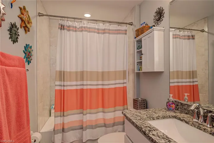 Full bathroom with vanity, shower / tub combo, and a textured wall