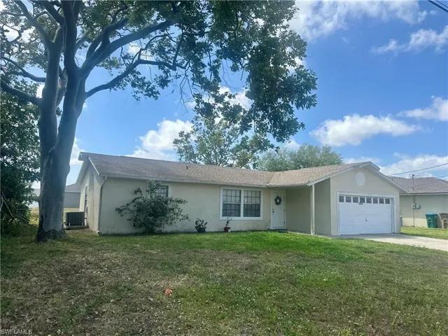 Ranch-style house with a front yard, central AC unit, an attached garage, stucco siding, and driveway