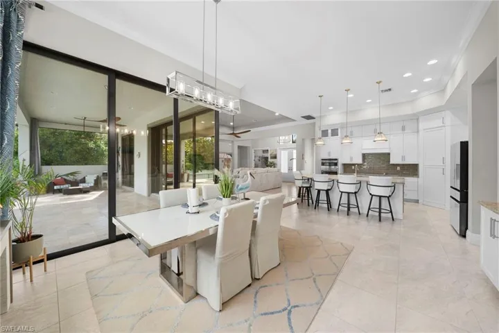 Expansive tile flooring throughout, featuring a modern kitchen with white cabinetry and stainless steel appliances, a breakfast bar with pendant lighting, and a dining area with a contemporary chandelier