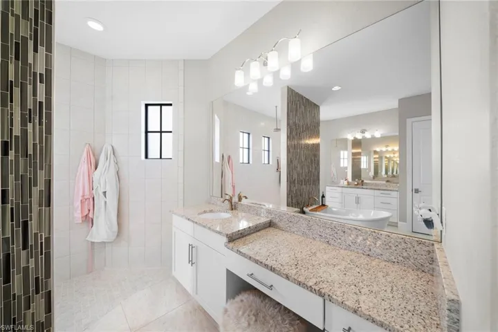 Spacious bathroom featuring a freestanding tub, dual vanity with granite countertops, and a large walk-in shower with mosaic tile accents