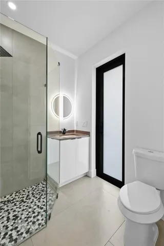 Bathroom featuring tile floors, a shower with door, oversized vanity, and toilet